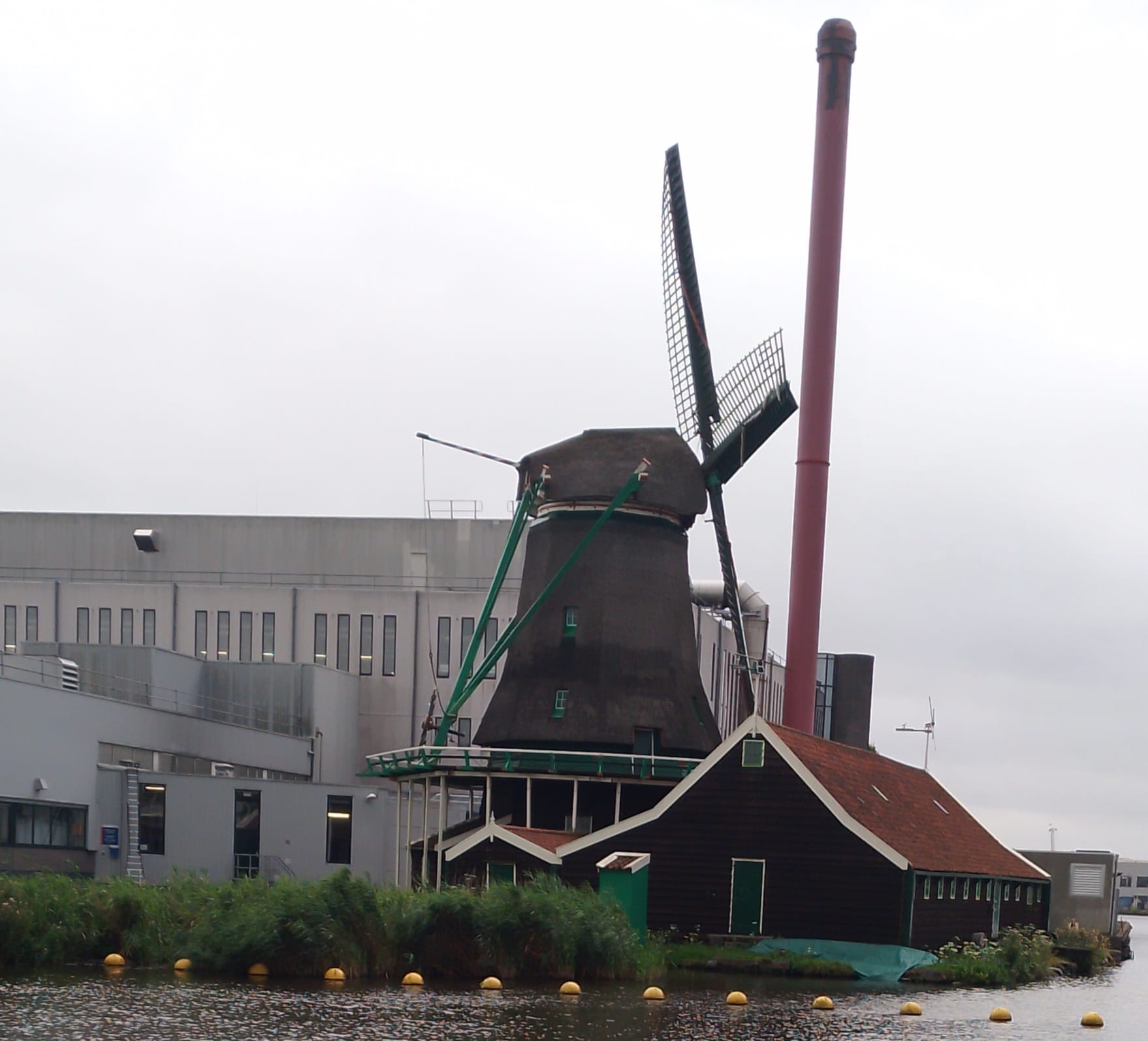 An Old fashioned Dutch windmill with an industrial factory behind it.